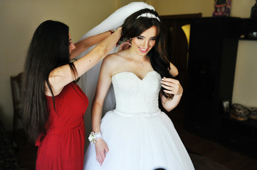 Happy cheerful brunette bride wearing at her room with two bridesmaids on red dress.