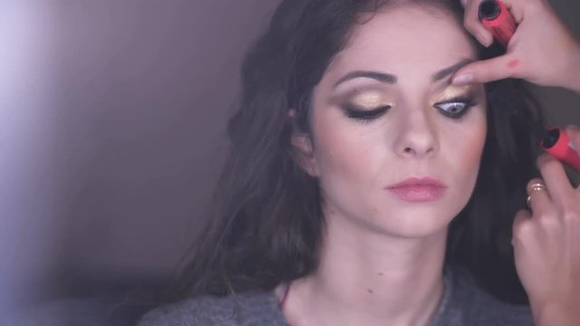 makeup artist applying mascara on cute young woman'eyes