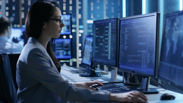 Female System Engineer Controls Operational Proceedings. In the Background People Working and Monitors Show Various Information.  Shot on RED EPIC-W 8K Helium Cinema Camera.