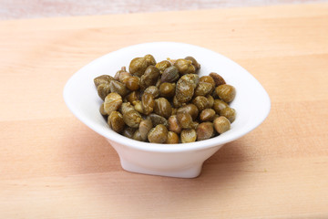 bowl with fresh capers on wooden table