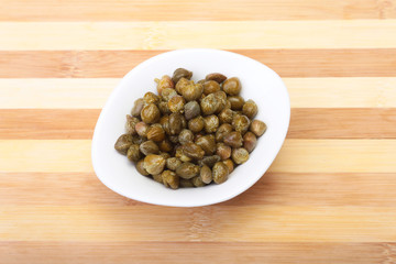 bowl with fresh capers on wooden table