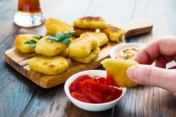 Portion of crisp chicken nuggets with tomato sauce and a glass of beer on the wooden table.