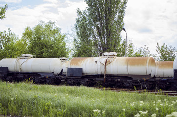 Fototapeta na wymiar Rusty Train Tankers Full Of Oil And Flammable Fluids Next To Green Grass