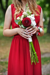 Cute girl bridesmaid at red dress with wedding bouquet at hand.