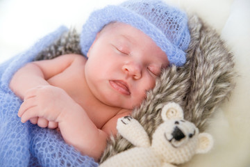 Sleeping newborn baby girl. Newborn baby in knitted cap and with a toy bear lying on a fur blanket.