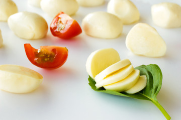Sliced mozzarella on a green leaf, slices of tomato and mozzarella balls on a white background
