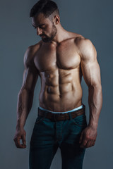 Muscle male model in jeans posing on blue background. Studio shoot.