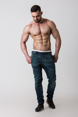 Fototapeta premium Muscle male model in jeans posing on white background. Studio shoot.