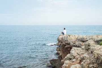 Fototapeta na wymiar Hombre joven sentado al borde de un acantilado al atardecer. Mar Mediterráneo
