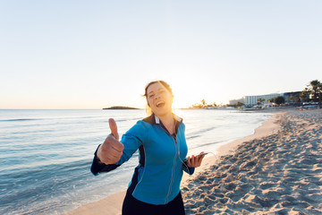 Concept of sport, fitness, healthy lifestyle and running - Motivated sporty woman doing thumbs up success gesture after outdoors workout at the beach