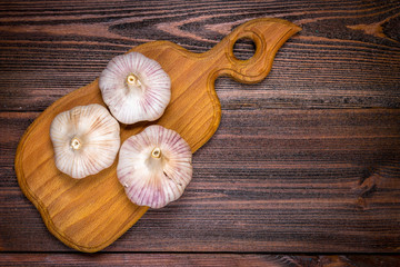 Garlic cloves and garlic bulb on a wooden board on a brown background. Top view