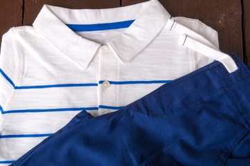 Blue shorts and white striped polo on brown wooden background. Boy outfit. Top view.