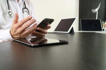 smart medical doctor working with smart phone and digital tablet and laptop computer on dark wooden desk in modern office