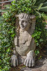 Obraz premium Statue of an Egyptian style half man half animal in a garden with ivy growing around it