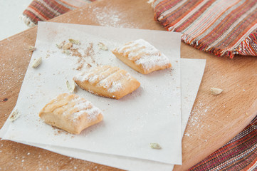 Fototapeta na wymiar Fresh pastry with various fillings sprinkled with powdered sugar on the wooden board. Selective focus
