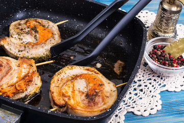 Fried meat on skewers in frying pan, blue background