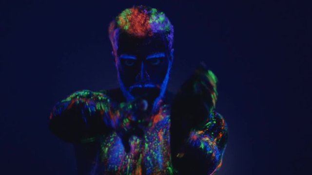 A man with a beard in the ultraviolet light. Magic passes with hands.