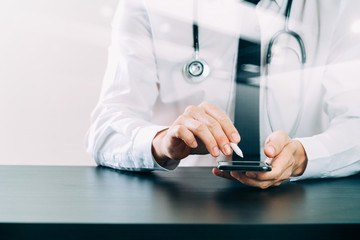 close up of smart medical doctor working with smart phone and stethoscope on dark wooden desk with virtual icon diagram