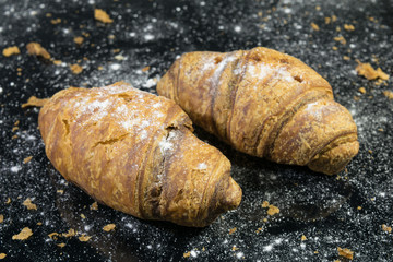 two croissants sprinkled powder on a black background