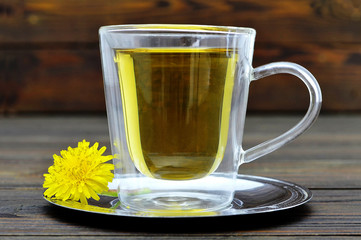 Dandelion tea in the transparent glass cup on wooden background