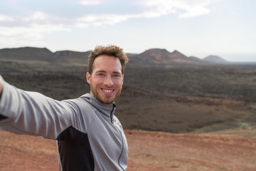 Travel tourist man taking selfie picture with smartphone hiking in volcano mountains of Lanzarote,...