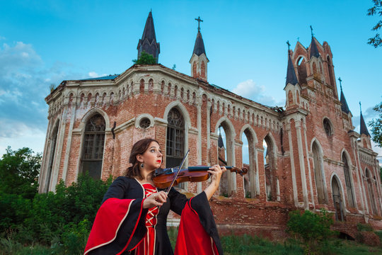 Woman musician playing the violin near an old castle
