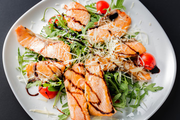 Fresh salad of salmon pieces, cherry tomatoes, lettuce, cheese and sauce on a white plate close up