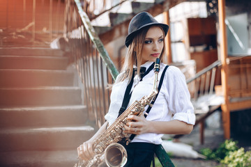 Young attractive girl in white shirt with a saxophone - outdoor in old town. Sexy young woman with sax thinking about something