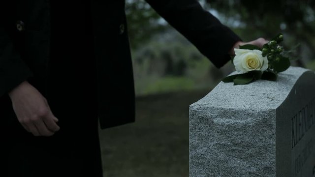 slow motion woman placing rose on top of grave stone in cemetary