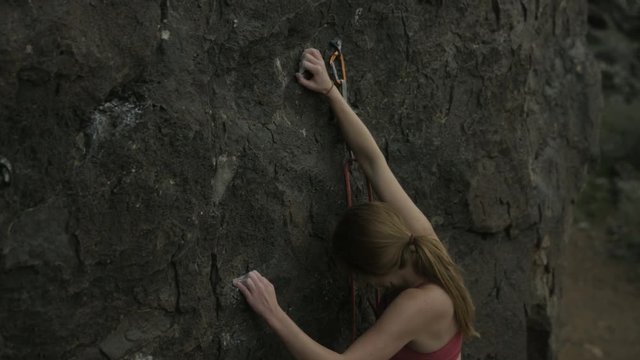 girl reaches for hold while rock climbing