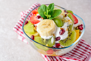 Fresh fruit salad with yogurt and walnuts in glass bowl on stone background.