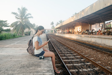 Fototapeta na wymiar Sri Lanka. Hikkaduwa. Girl tourist with the phone in her hands crouched on the edge of the platform in anticipation of the train
