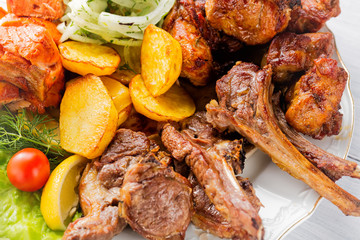 Grilled meat, ribs, grilled salmon fish, potatoes, herbs and tomato on white plate and white wooden table. Close up with selective focus