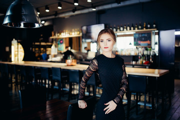 European-looking girl in a black evening dress at the restaurant welcomes guests.