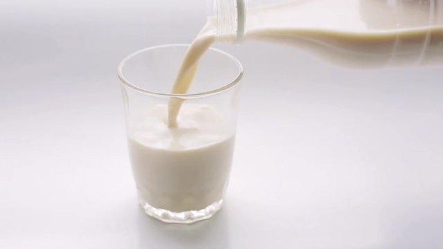 Pouring milk in a glass cup on a white background.
