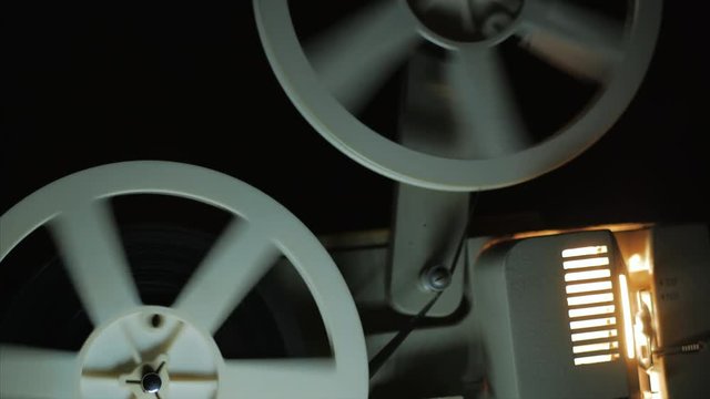 Old 8mm film projector playing in the night. Close-up of a reel with a film. 4k