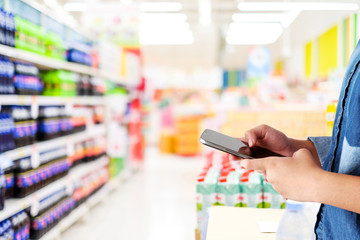 Naklejka na ściany i meble Hand holding smart phone over blur supermarket store background, online shopping, digitalmarketing, e-commerce, business and technology background, template
