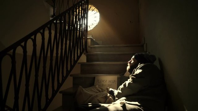 Lonely homeless lying on the shaded stairs is lit by morning light