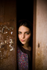 Fototapeta premium A young curious girl looks out from behind the door of her house. She thinks about going outside. agoraphobia concept