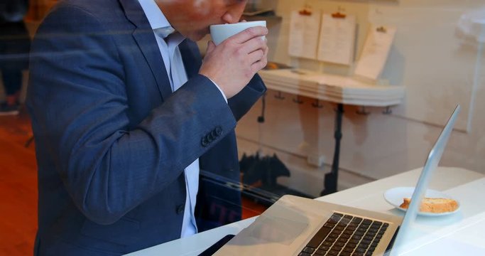 Businessman using laptop while having cup of coffee