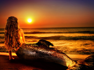 Water nymph mermaid woman dreams on sea sandy beach. Fairy nixie girl looks at tropical setting sun. Fantasy sunset painted undine, sky and sea waves in gold. Magical fish tail of naiad shining squama