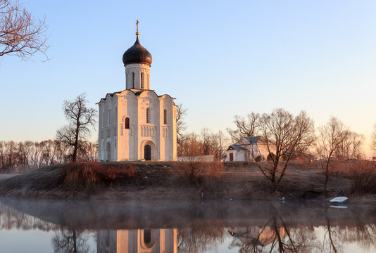 A misty lake with a boat in front of the church in the early spring at dawn