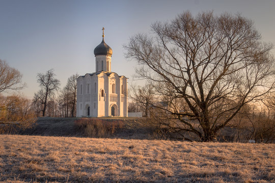 The frost on the grass blazes in the rays of the cold, blooming sun, beautifully outlining the silhouettes of trees and an ancient church