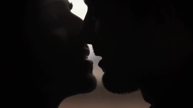 Close up on Silhouette of men kissing in the mouth