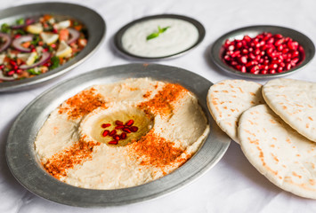 Hummus, tabbouleh, and Arab pita bread with pomegranate seeds and white sour cream sauce against white background. Selective focus.
