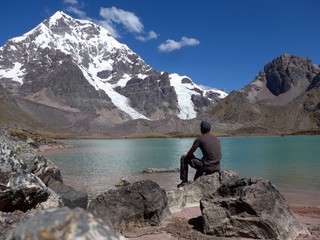 Man sitting by a beautiful shallow emerald and pink lake in the high Andes of Peru on a beautiful...