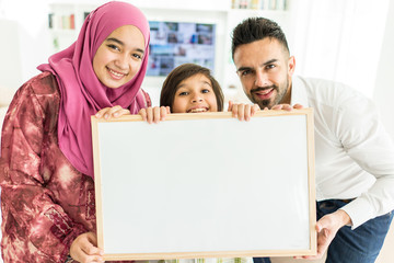 Happy Arabic Muslim family at modern home having fun and good time together holding white board for copy space message