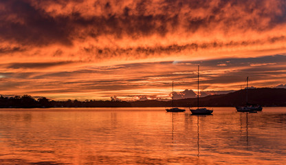 Fototapeta na wymiar Boats on the Bay with an Orange Cloudy Sunrise