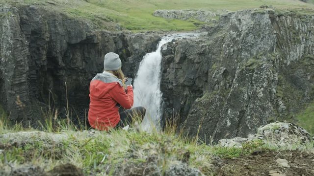 woman taking photo of waterfall with her cell phone