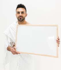 Muslim man posing as ready for Hajj visiting Kaaba in Mecca holding white board for copy space your text or image